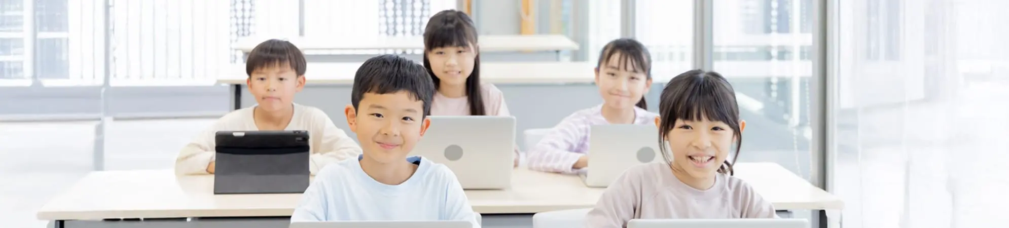 小学生の男女5名がタブレットやPCで楽しく勉強しています