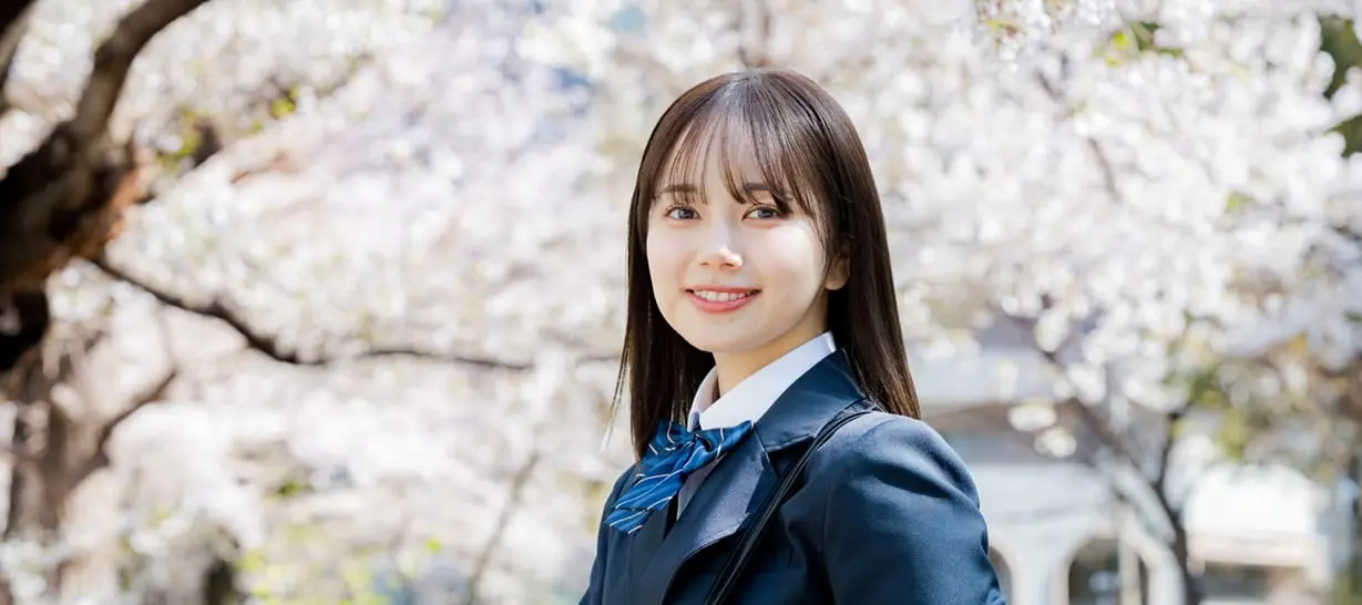 女子生徒が桜並木をバックに笑顔で立っています