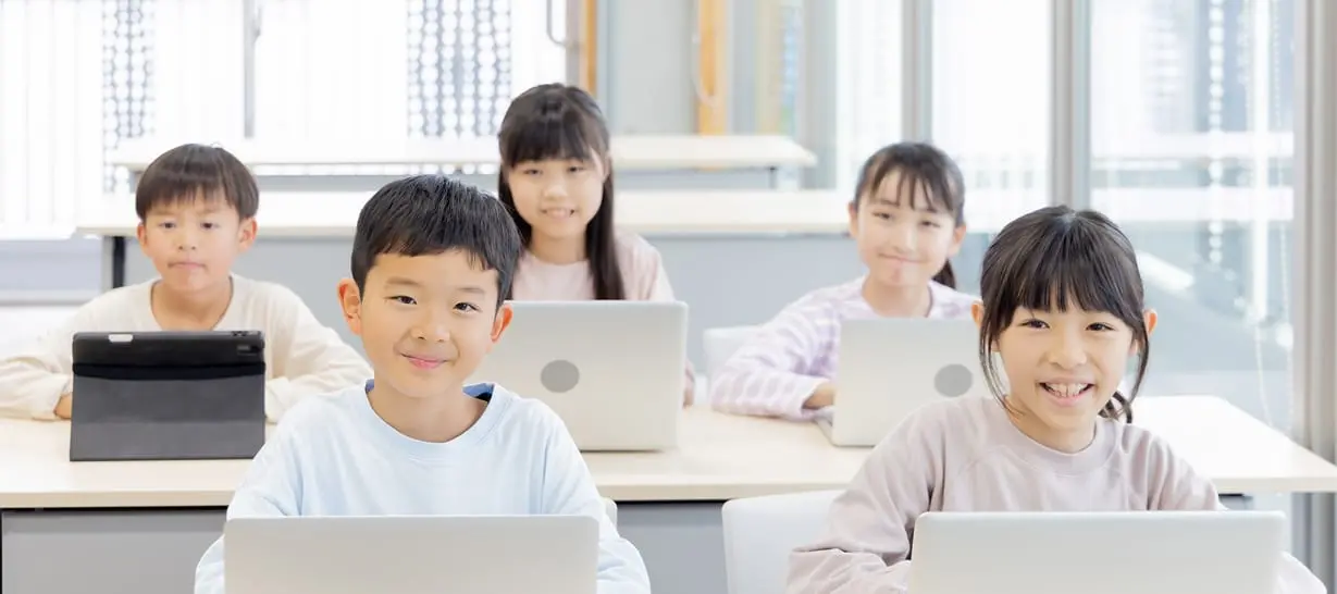 小学生の男女5名がタブレットやPCで楽しく勉強しています