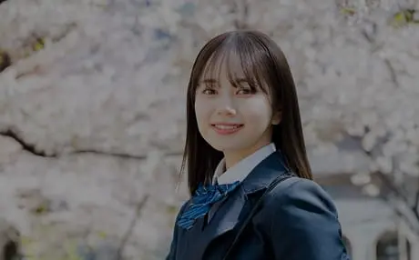 女子生徒が桜並木をバックに笑顔で立っています
